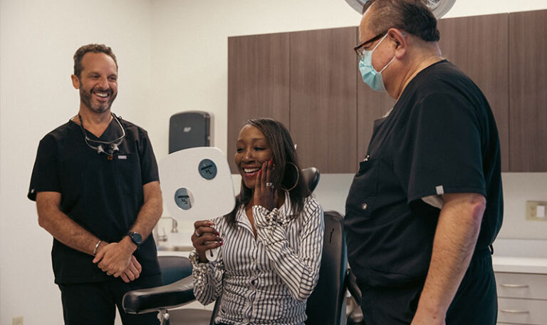 Smiling dental patient checking results in mirror with dentists at Dr. Friedberg & Associates in Houston