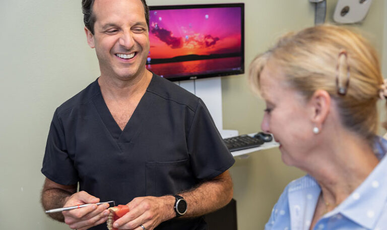 Dr. Friedberg explaining dental treatment options using a model during a consultation with a smiling patient