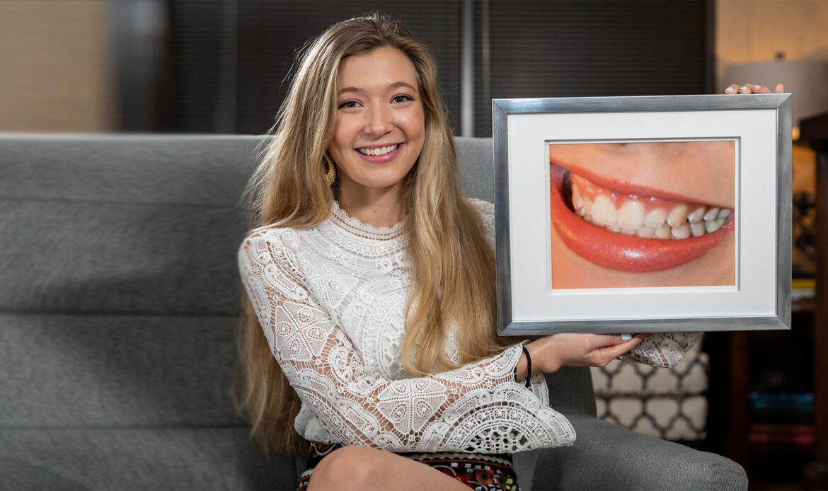 Smiling female patient holding a framed photo of her gum treatment before and after at Dr. Friedberg & Associates
