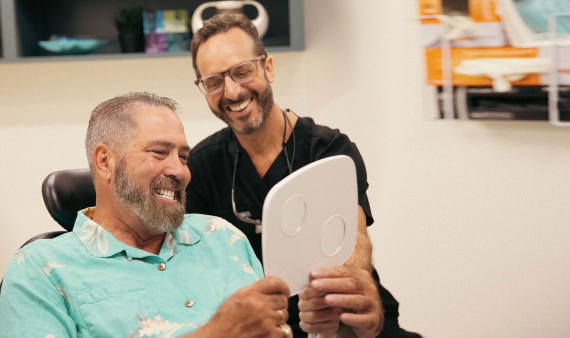 Happy dental implant patient smiling with Dr. Friedberg while viewing new smile in mirror
