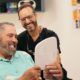 Happy dental implant patient smiling with Dr. Friedberg while viewing new smile in mirror