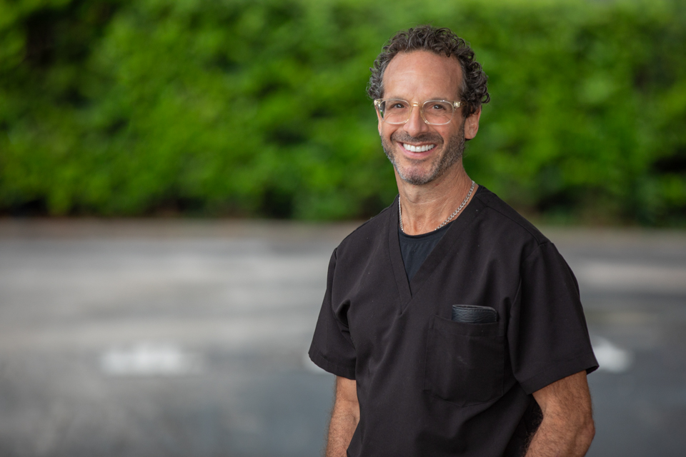 Dr. J. Robert Friedberg, board-certified periodontist in Houston, smiling in black scrubs outdoors