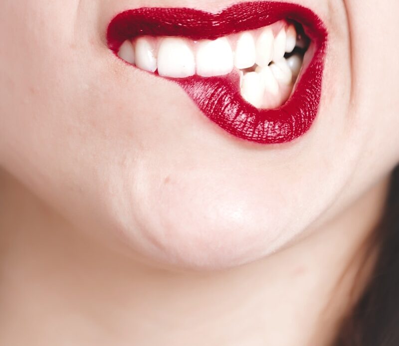 close-up photo of a smiling person wearing red lipstick showing healthy teeth
