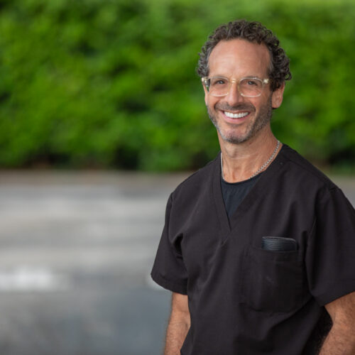 Dr. J. Robert Friedberg, board-certified periodontist in Houston, smiling in black scrubs outdoors